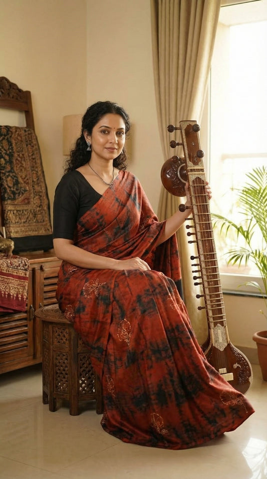 Woman wearing a Ajrakh Modal Silk Saree – Red & Black Tie-Dye with Black Pallu holding a sitar in a room with decorative items.