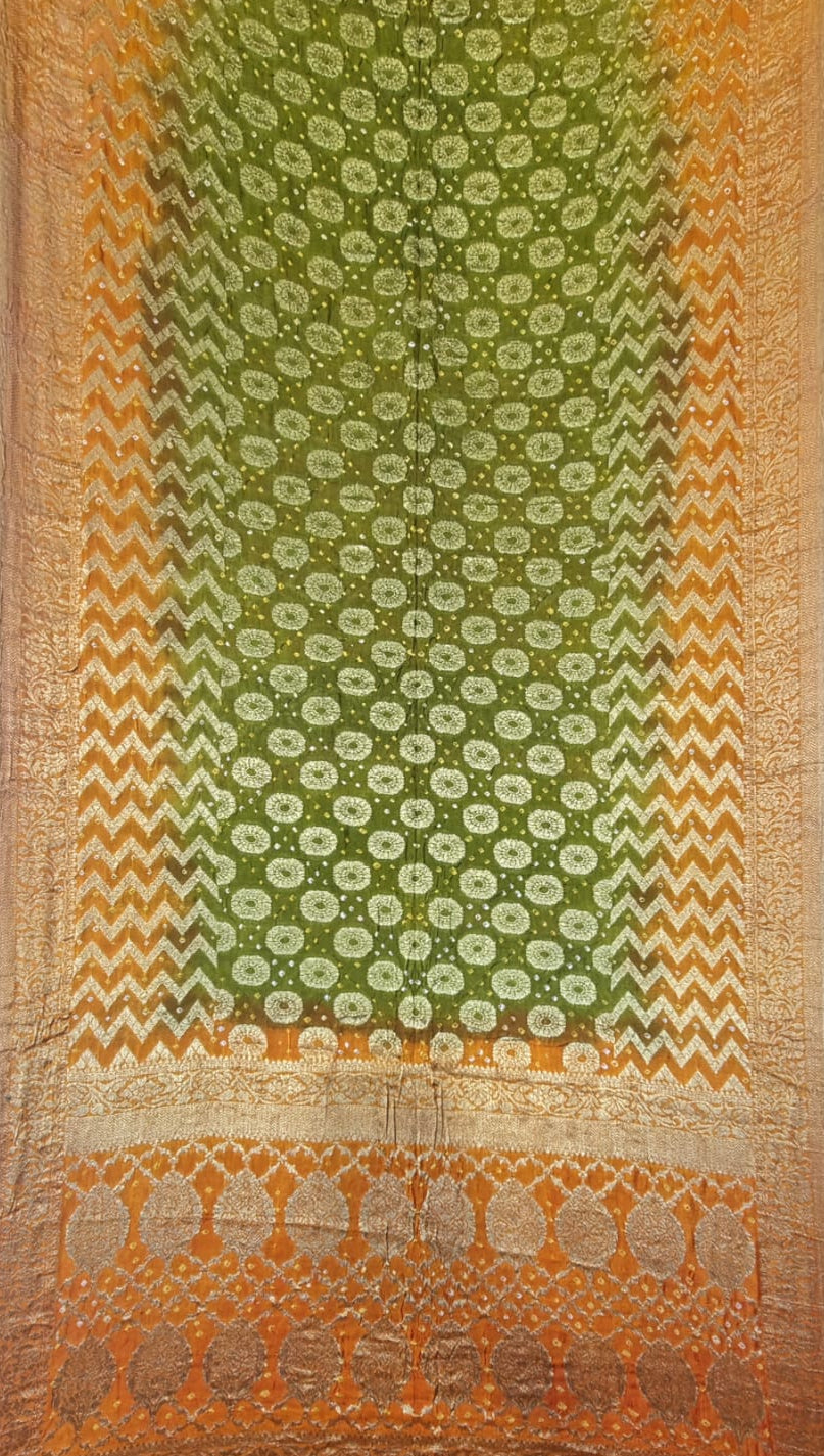A traditional Indian art silk saree displayed flat, featuring a green body with intricate gold floral patterns, a wide orange and gold chevron border, and a decorative gold zari border at the bottom.