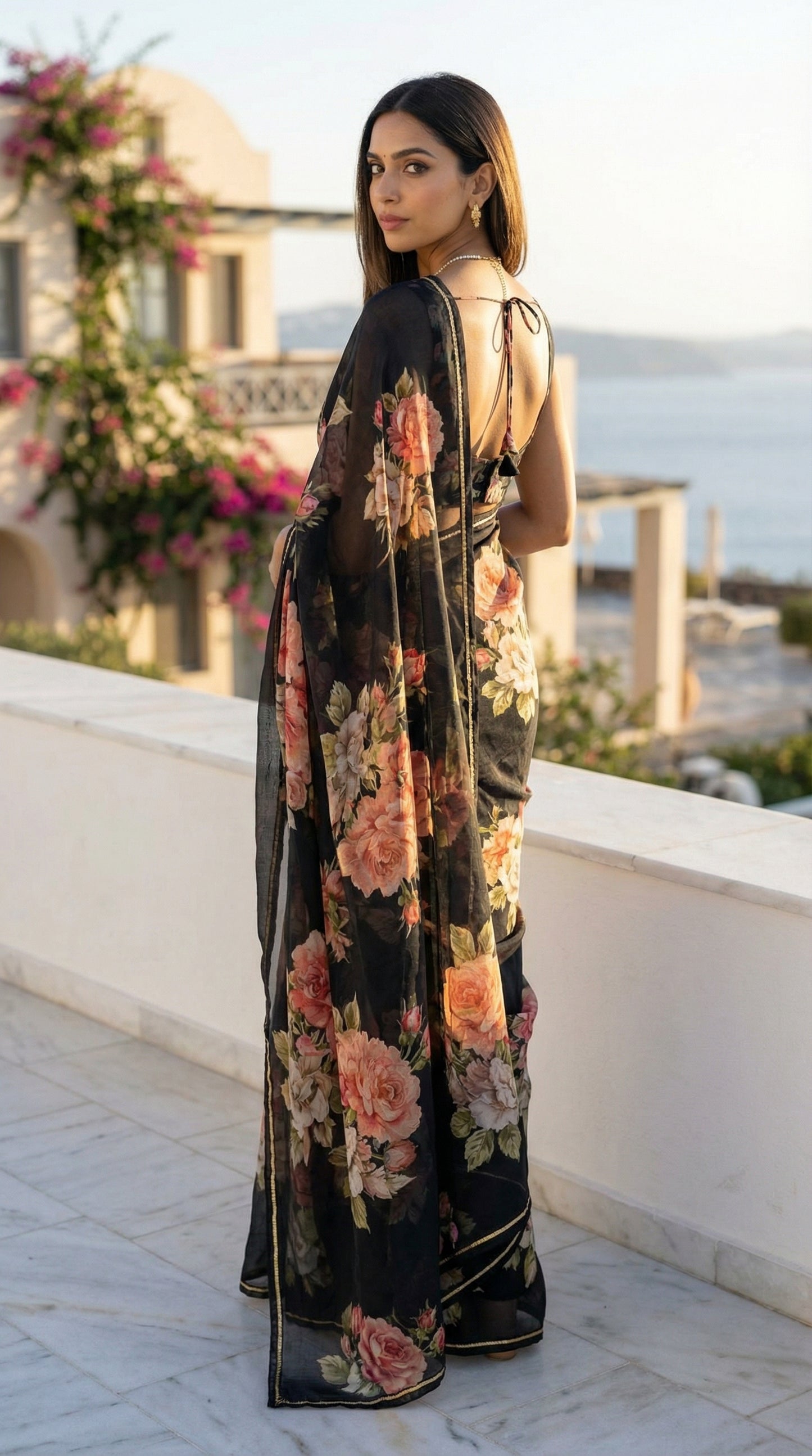 Woman wearing a black chiffon saree with floral prints, with a scenic background.