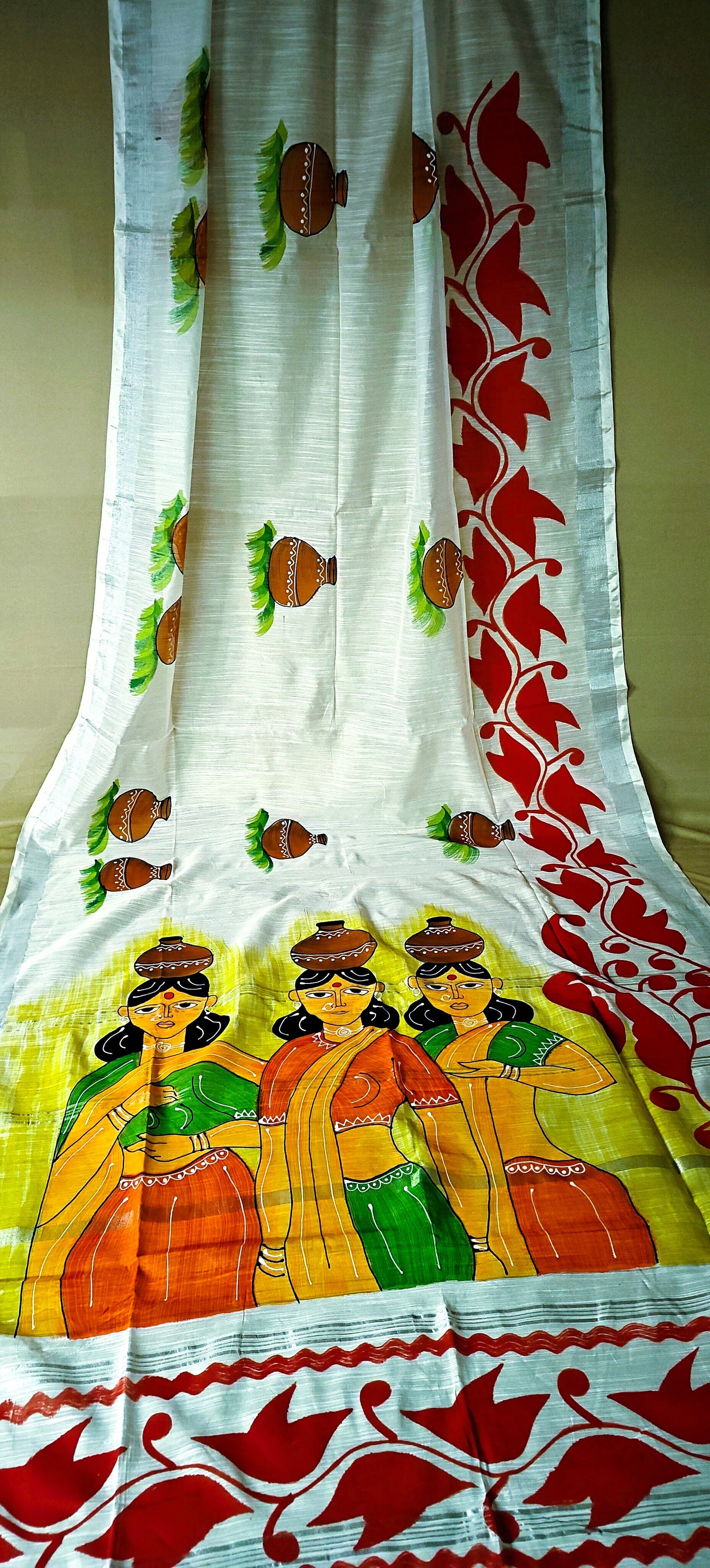 White cotton saree with hand-painted design of three women in traditional attire and ritual pots, artisan ethnic wear.