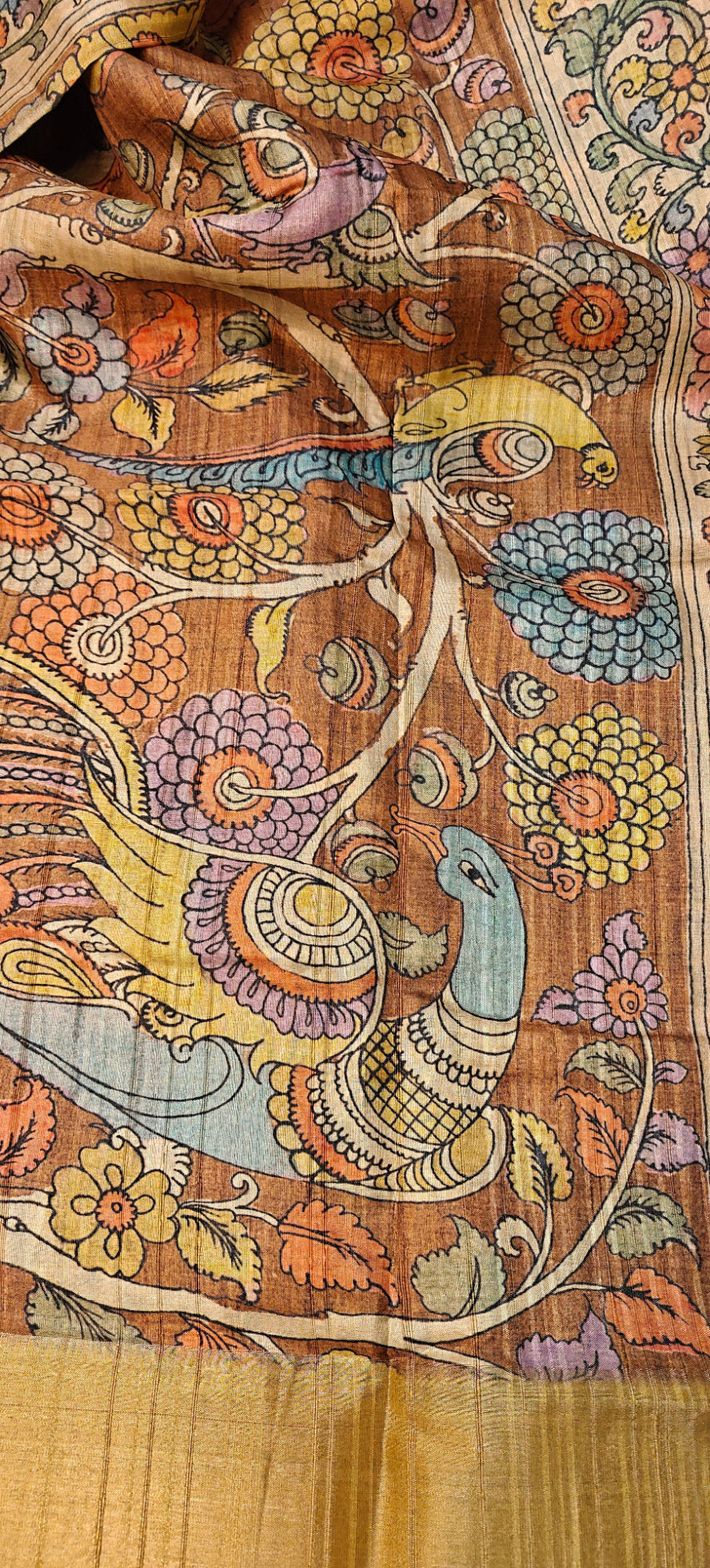 Blue saree with Kalamkari-inspired floral vine digital print and golden border lying flat and folded on a beige background with flowers.