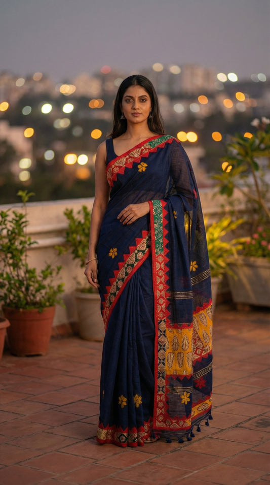 Woman in a midnight indigo linen cotton saree with handcrafted applique border, on a rooftop with city lights in the background.