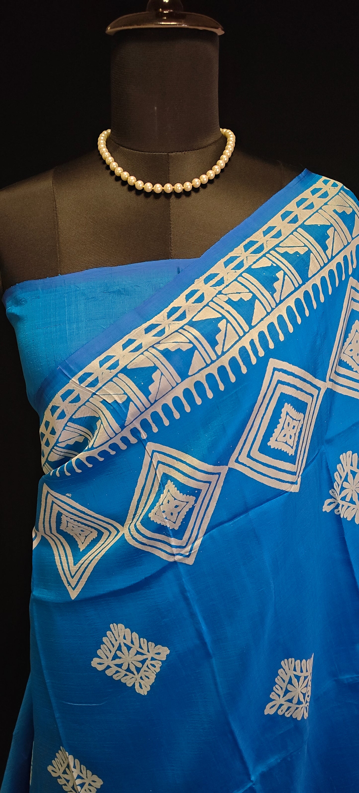 Pure bishnupuri silk saree in royal blue with white digital print motifs and geometric border, styled on mannequin showcasing the plain blue blouse piece against black background.