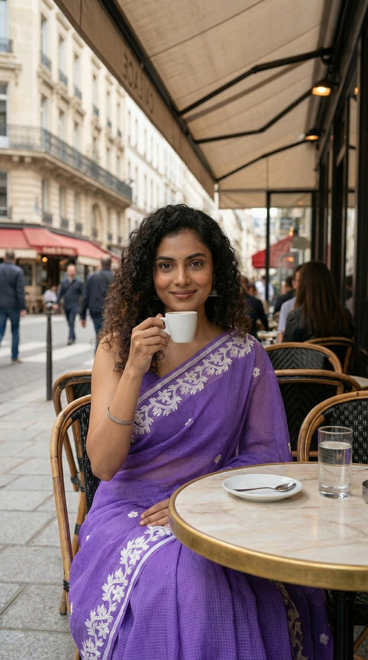 Woman in a purple-kota-doria-saree, drinking coffee at an outdoor cafe in an urban setting