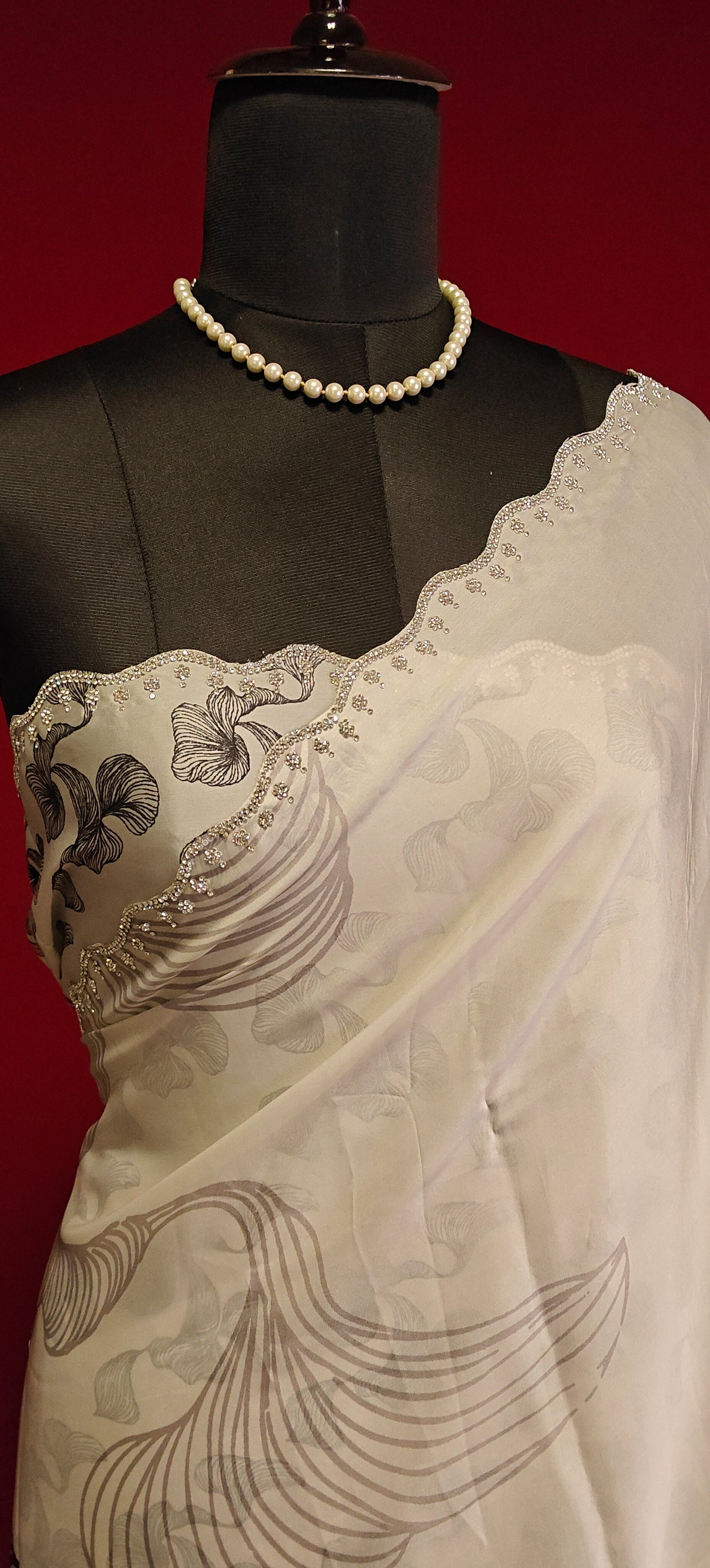 White satin saree with black abstract design and silver motif border, styled on mannequin showcasing the blouse piece against red background.