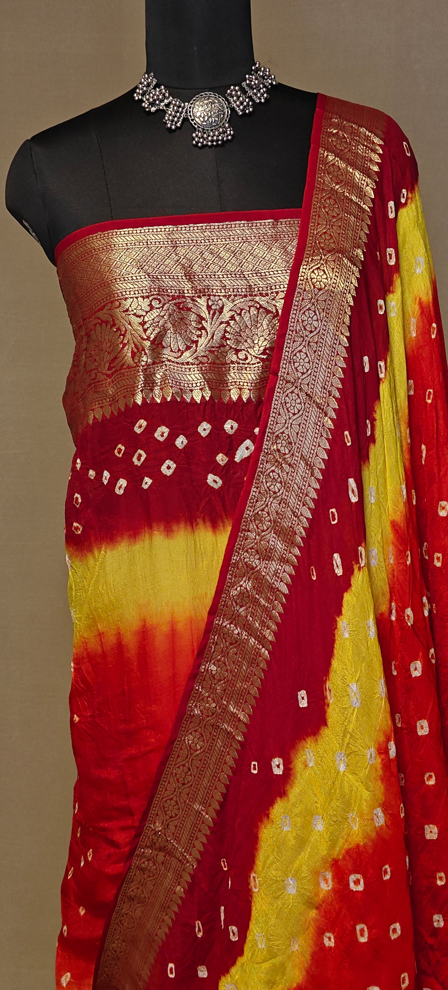 Red and yellow silk saree with floral arrangement on a mannequin against a neutral background.