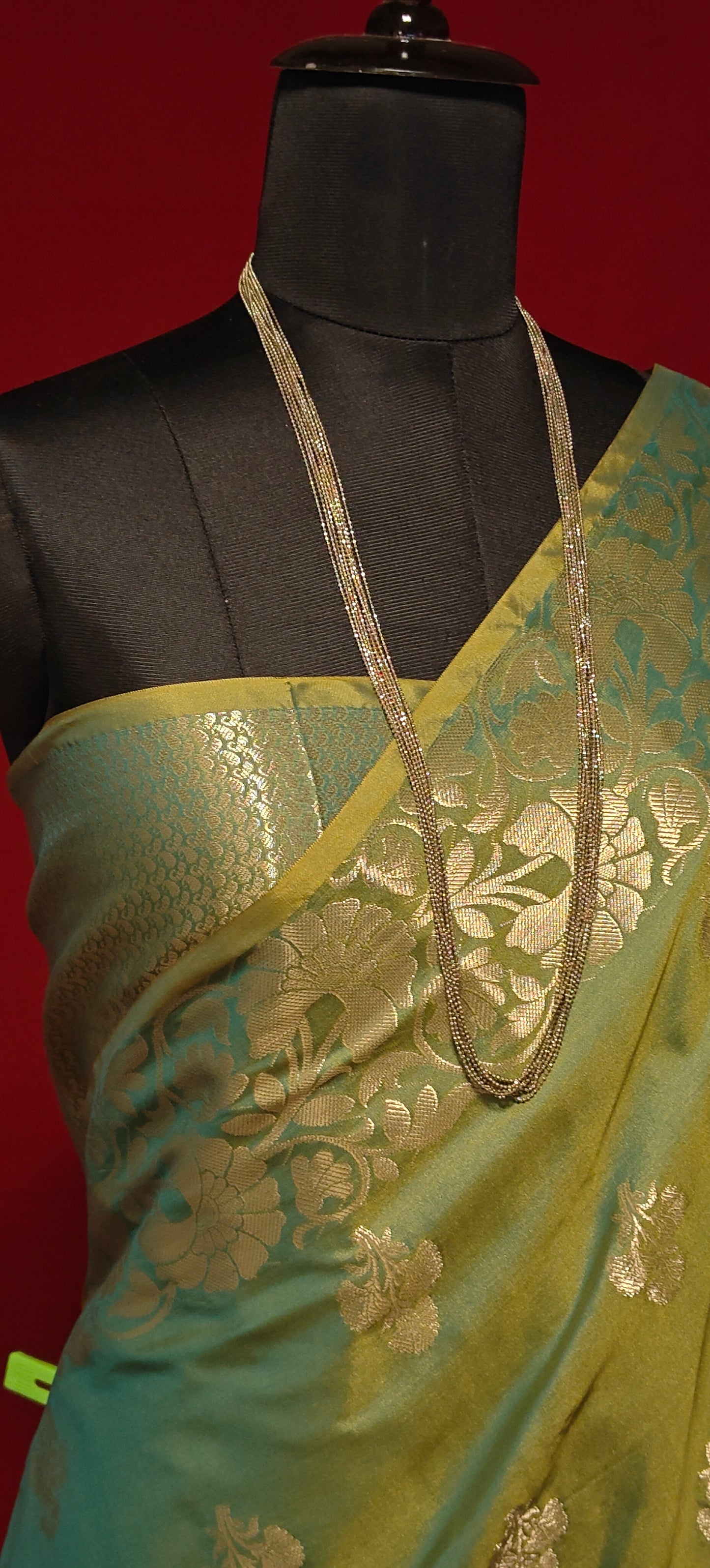 Emerald green silk blend saree with intricate woven detailing and elegant drape on a mannequin against a red background