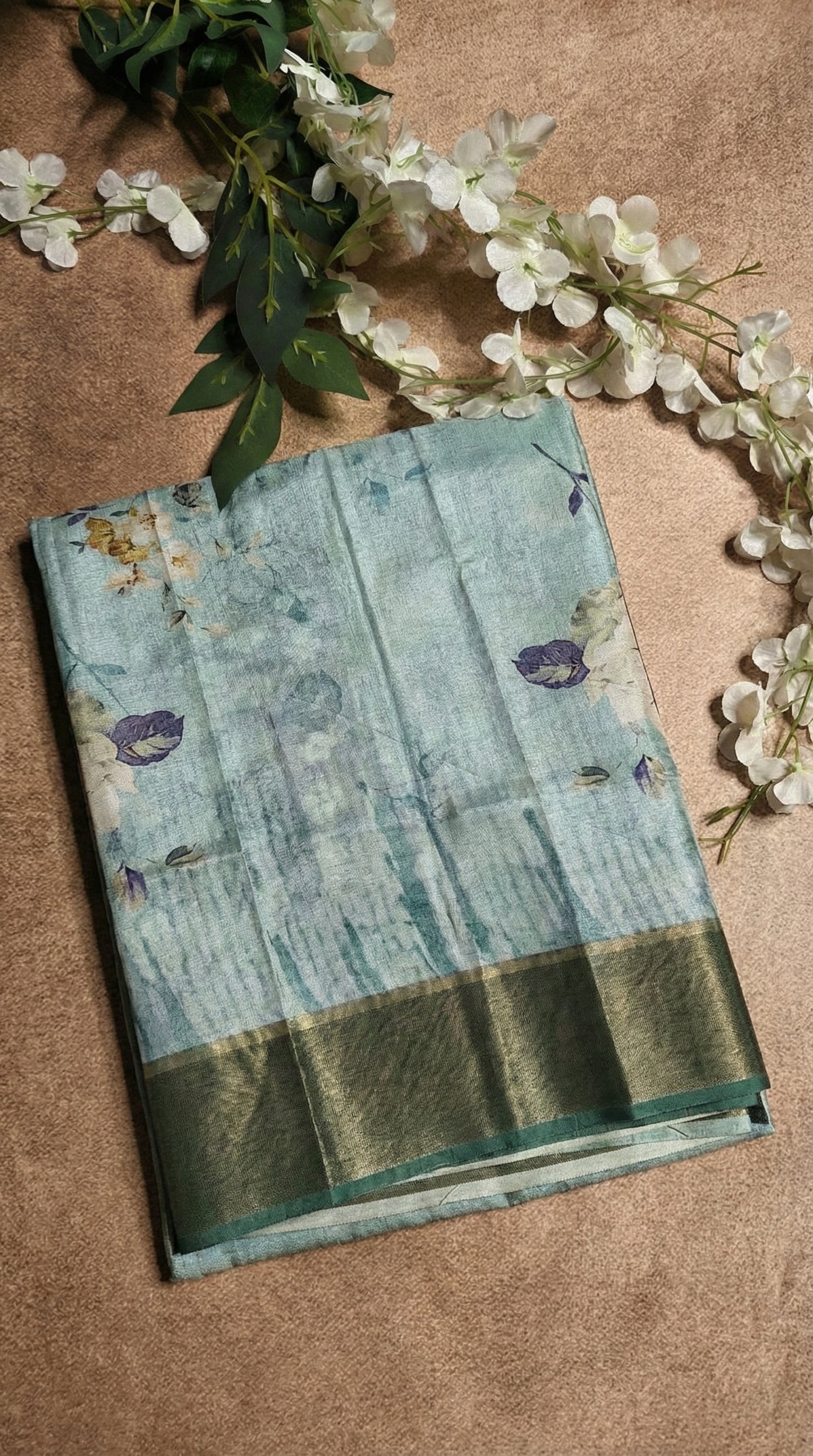 Sea green viscose silk saree with floral print lying on a flat surface with flowers.