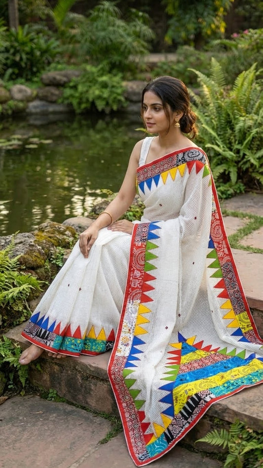 Woman in a white cotton saree with vibrant multi-color triangle appliqué and geometric printed borders with colorful patterns sitting by a pond.