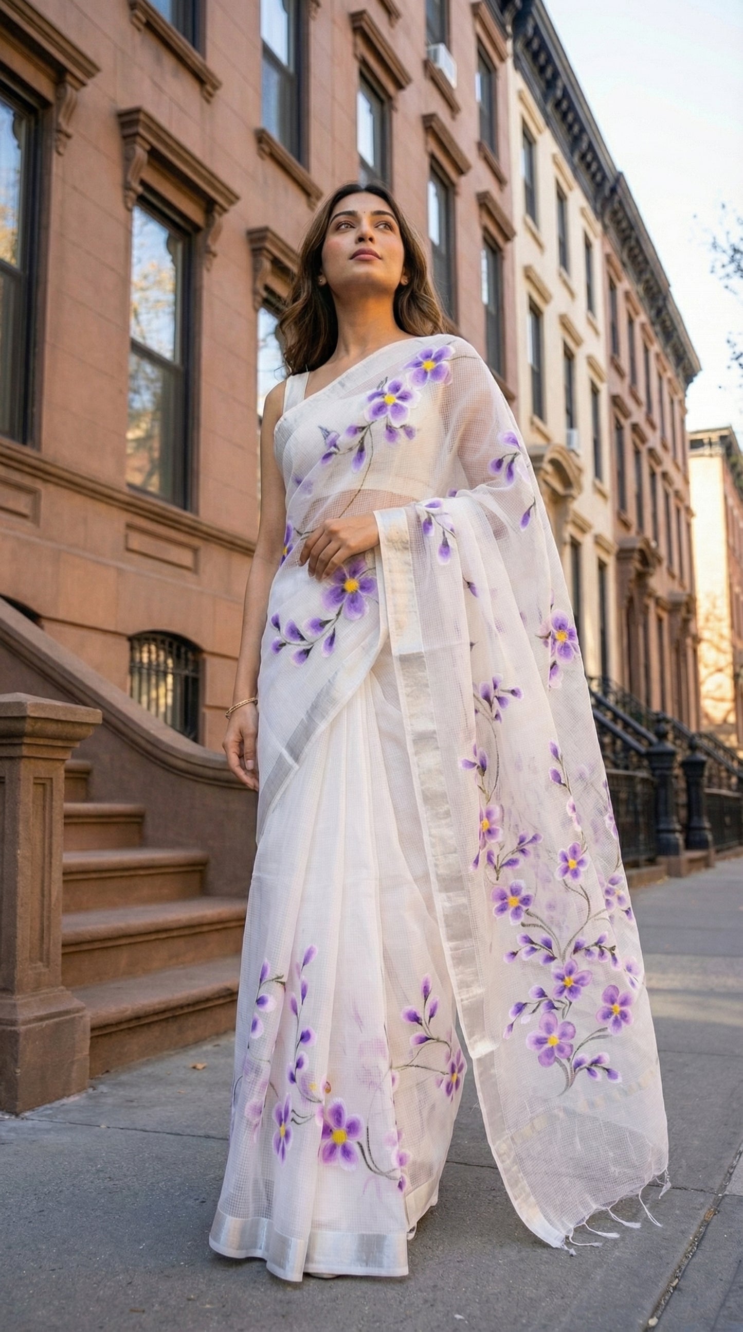 Woman wearing a white-lilac-hand-painted-kota-saree, floral patterns standing on a city street.