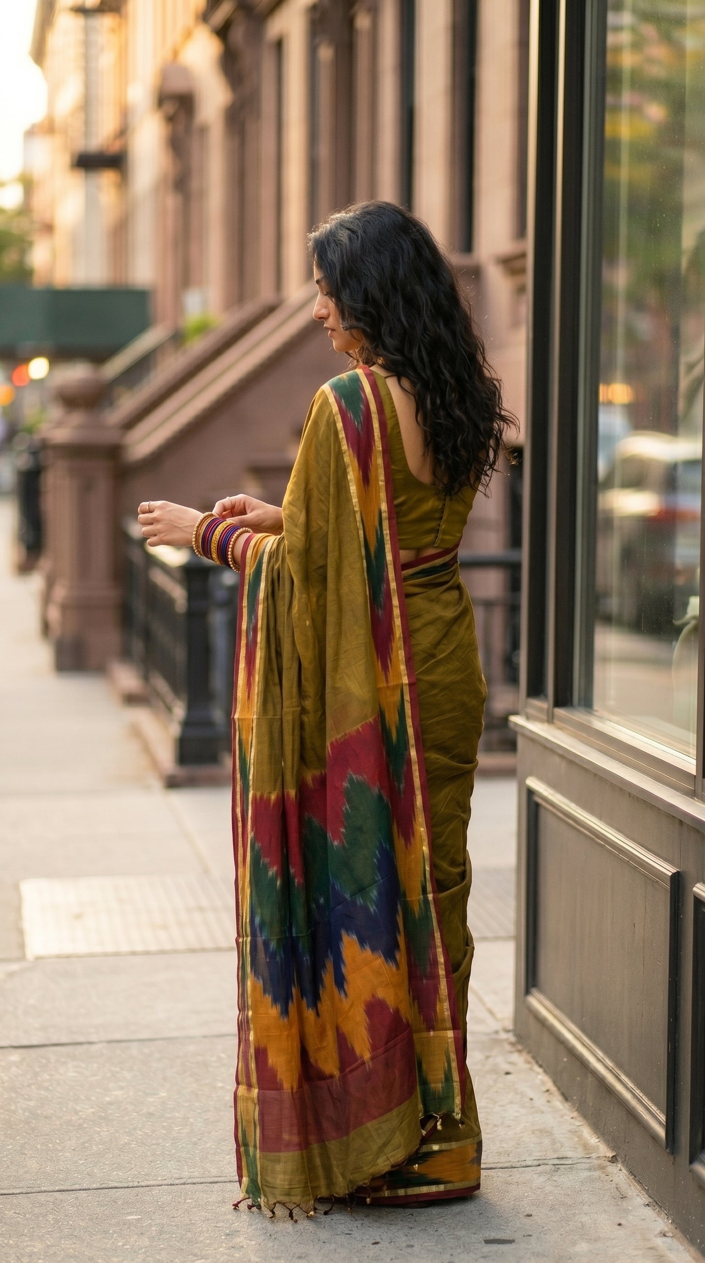 Woman in a handloom cotton saree with ikat border – antique golden with magenta yellow and green border walking on a city street.