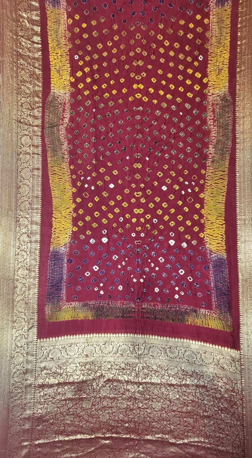 A Art Silk Bandhani with Shibori & Zari Border - Maroon saree, decorated with rows of small yellow, blue, and white mirror work (chikankari) motifs, framed by wide gold Zari borders.