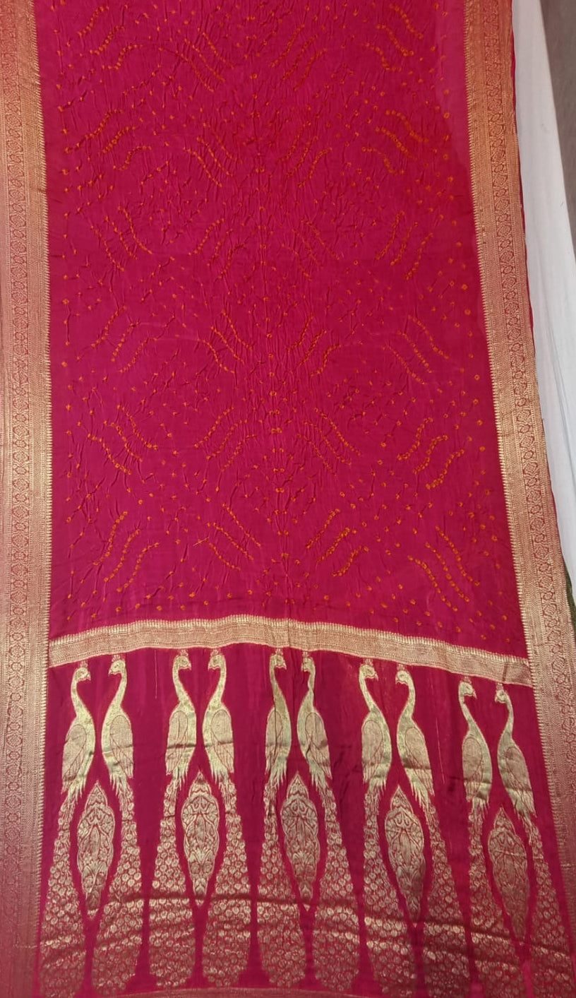 A close-up of a Art Silk Saree with Multi Bandhani - Red, featuring intricate gold Zari woven patterns and a decorative border with peacock motifs.