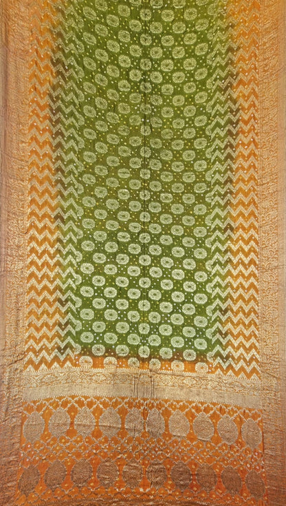 A traditional Indian art silk saree displayed flat, featuring a green body with intricate gold floral patterns, a wide orange and gold chevron border, and a decorative gold zari border at the bottom.