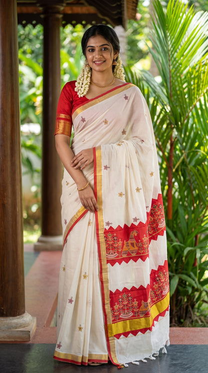 Full-length portrait of a smiling woman standing under a wooden pavilion next to tropical greenery, displaying the full front profile of a white and red Kerala cotton saree