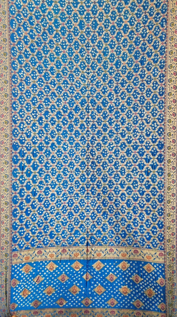 A blue patterned art silk saree with an intricate repeating floral motif and a decorative border, shown flat against a neutral background.
