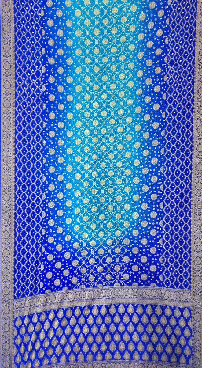 A blue and turquoise gradient art silk saree with intricate silver metallic patterns, featuring a wide decorative border at the bottom.