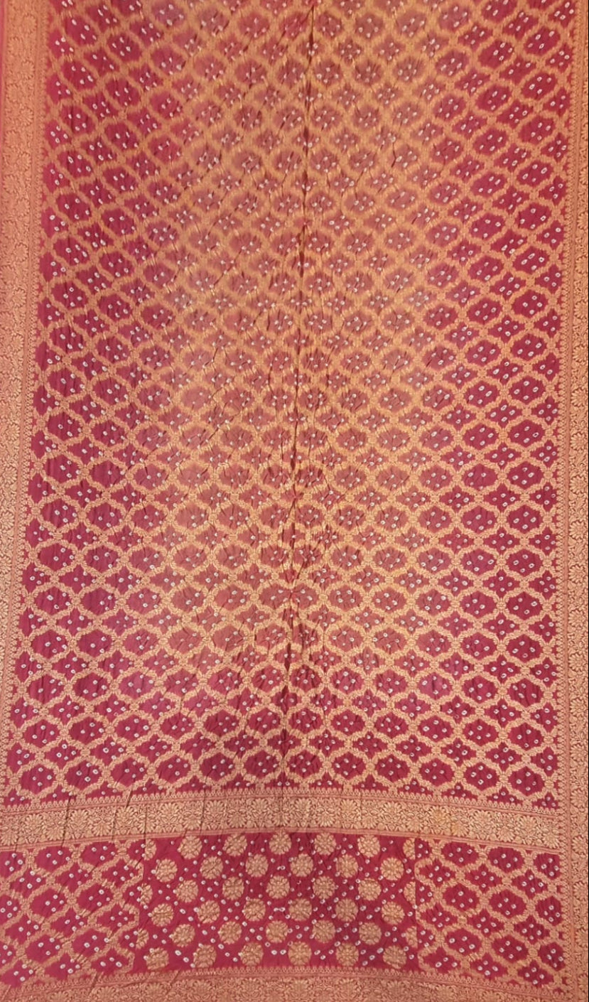 A close-up of a red and gold patterned art silk saree, featuring a repeating diamond motif and a decorative border.