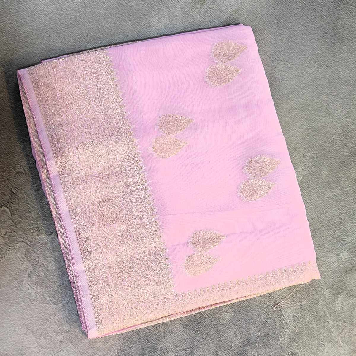 A folded Georgette Saree with Banarsi Border-Pink, displayed on a textured gray surface.
