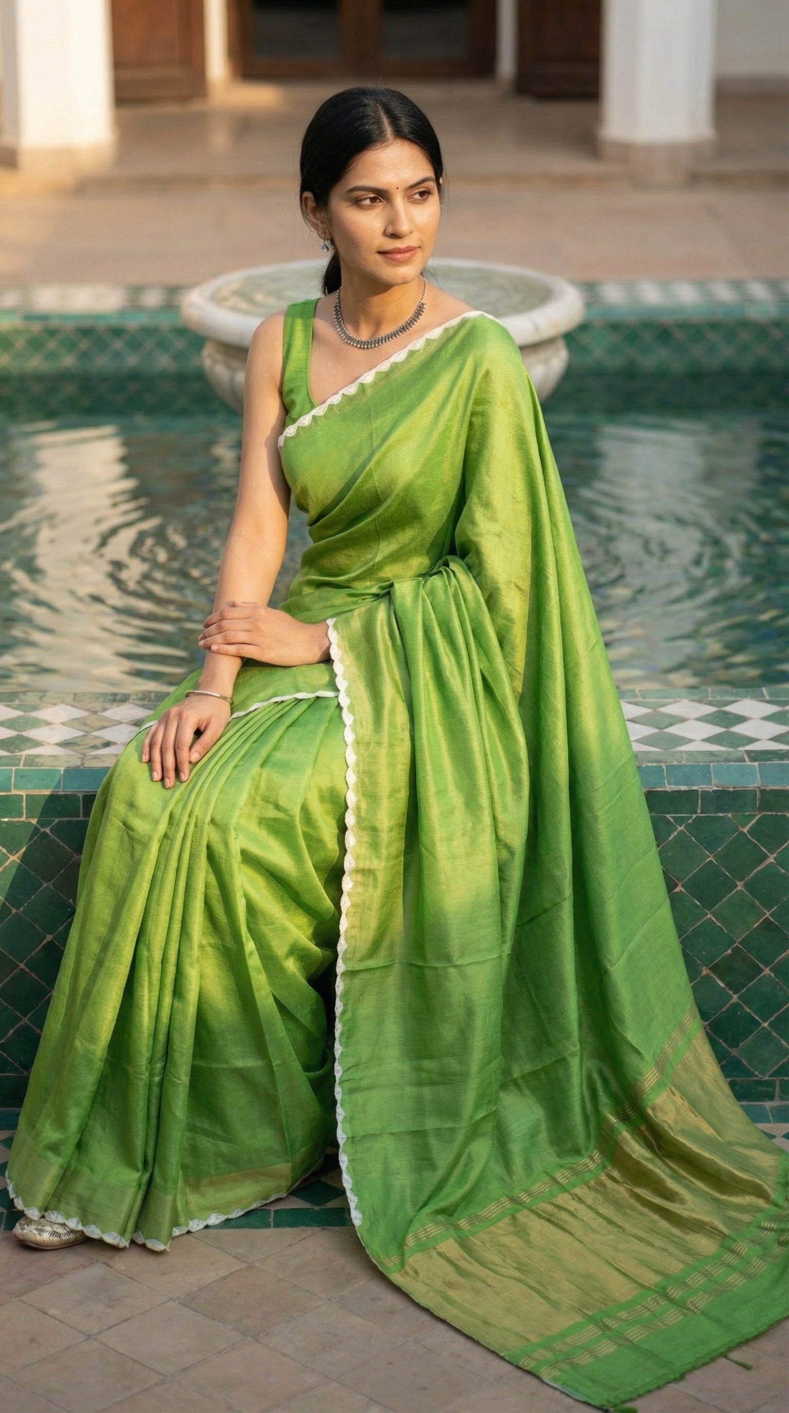 Woman wearing Green Modal Silk Saree with Lagdi Patta Pallu saree with white border, sitting near a fountain.