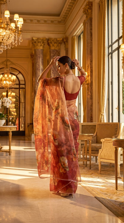 A woman adjusts her hair in a grand palace hallway, showcasing the sheer back drape of a rust brown floral printed chiffon saree