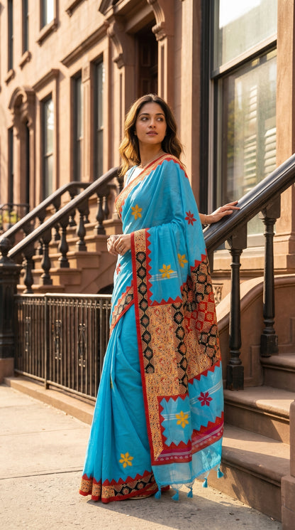 Model looking over her shoulder while posing on brownstone stairs with a black metal railing, highlighting the bright red zigzag trim and detailed geometric applique borders of her blue saree