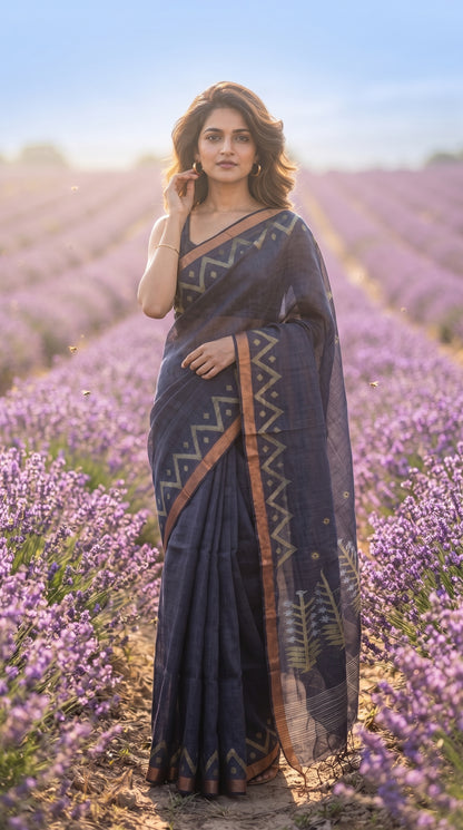 Full-length editorial portrait of a woman standing in a purple lavender field while touching her earring, highlighting the elegant straight silhouette and geometric zari lines of her deep steel-blue linen saree