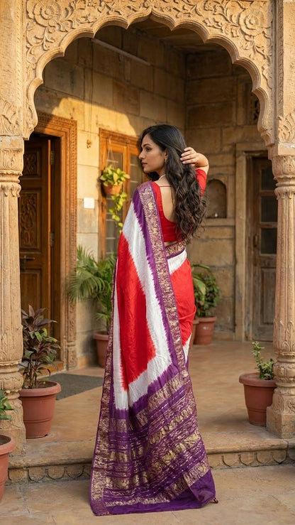 Woman in a magenta modal silk saree with purple zari border standing in front of an architectural entrance.