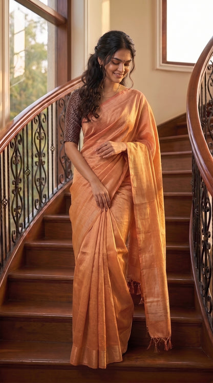 A full-length portrait of a smiling woman descending an indoor wooden staircase with decorative iron railings, displaying the structured, high-volume drape of her rose gold tissue cotton saree