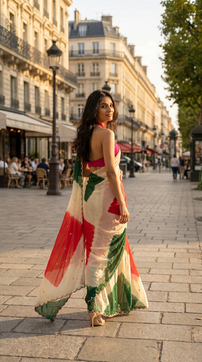 A woman wearing an ivory chiffon saree with red and green tie-dye blocks looking over her shoulder on a historic European street