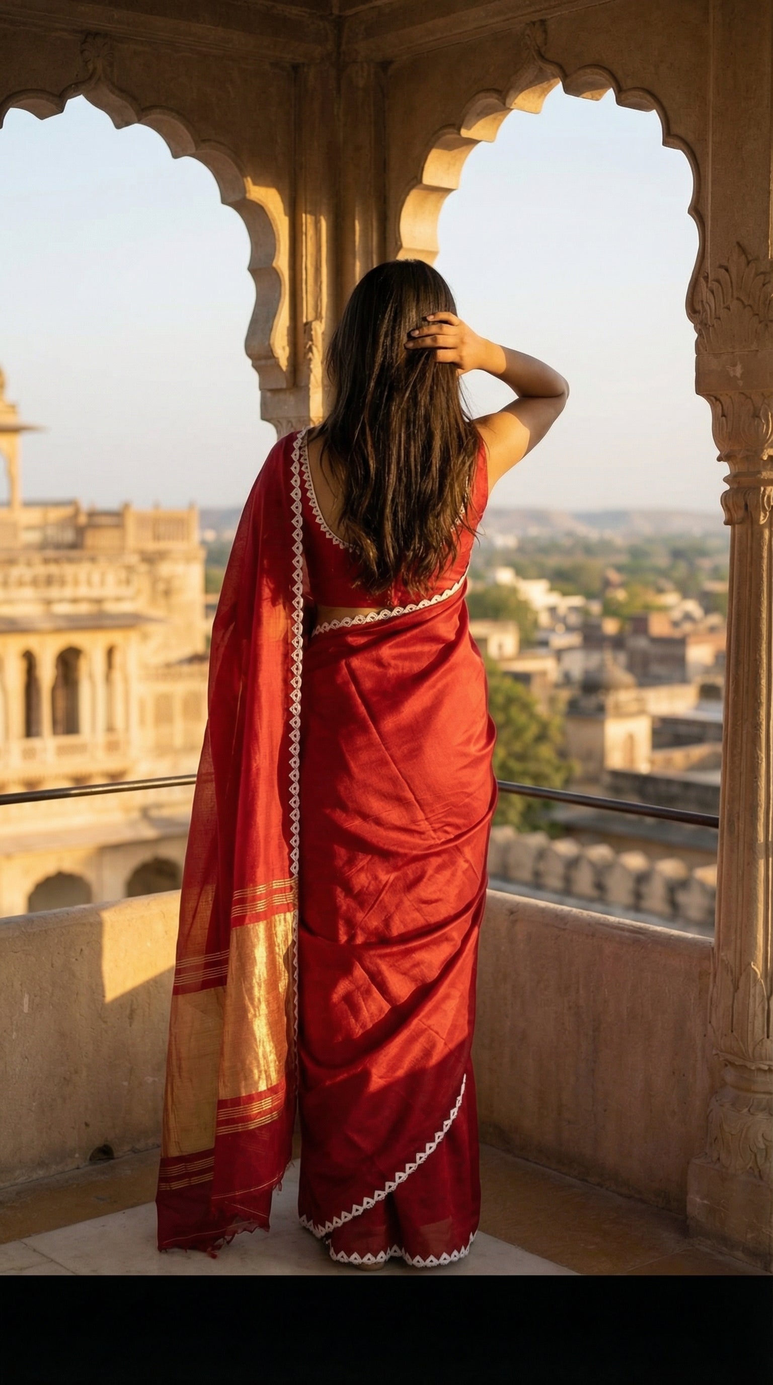 Woman in a red Modal Silk Saree with Lagdi Patta Pallu saree with white border, standing on a balcony with a scenic view.