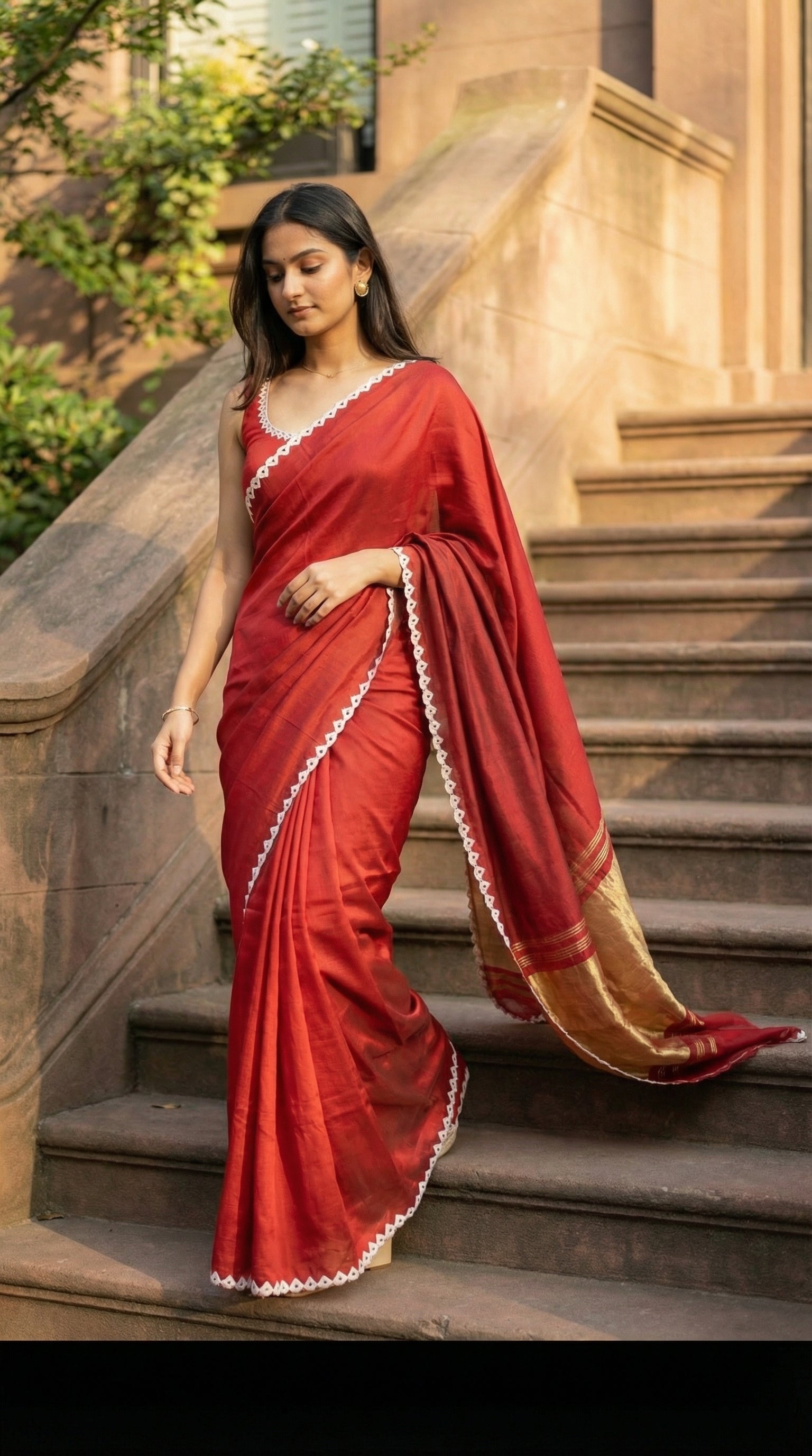 Woman in a red Modal Silk Saree with Lagdi Patta Pallu saree with white border, standing on stone steps outdoors.