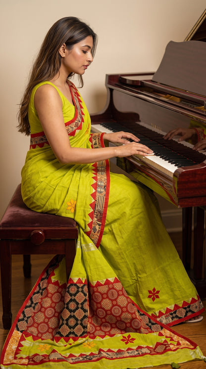 Model seated on a piano bench playing a grand piano, elegantly displaying the fluid fall, star embroidery, and heavy red geometric pallu of a lime green cotton linen saree