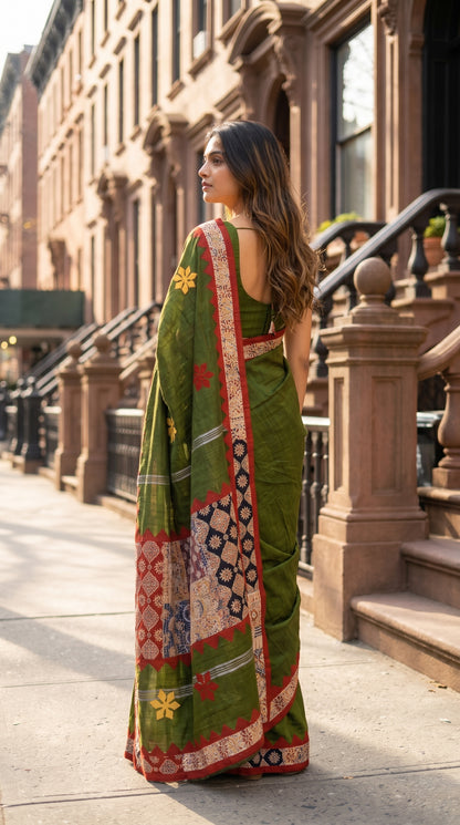 Three-quarter back view of a woman walking past brownstone buildings, showcasing the detailed multi-patterned geometric patchwork pallu of an olive green saree
