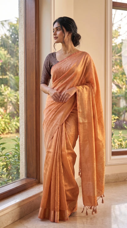 A full-length front portrait of a woman standing by a large glass window overlooking a garden, beautifully showcasing the flawless tailored silhouette and subtle metallic shimmer of her rose gold tissue cotton saree
