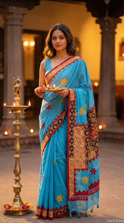 A woman standing next to a tall brass diya stand while holding an aarti plate, elegantly showcasing the front look and yellow star patterns of a sky blue cotton linen saree