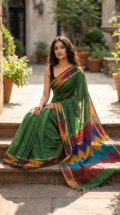Woman in a handloom cotton saree with ikat border – green with magenta, yellow and green border sitting on steps outdoors.
