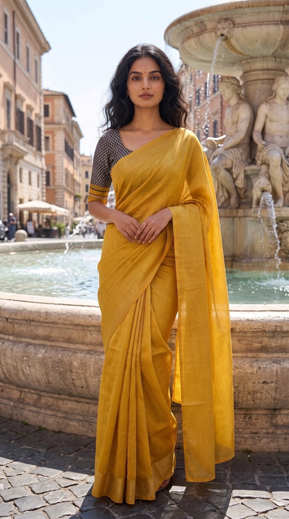 A full-length front portrait of a woman standing near a grand historic stone fountain, displaying the sophisticated solid canvas, clean structured pleats, and subtle gold glaze of her yellow-golden tissue cotton saree