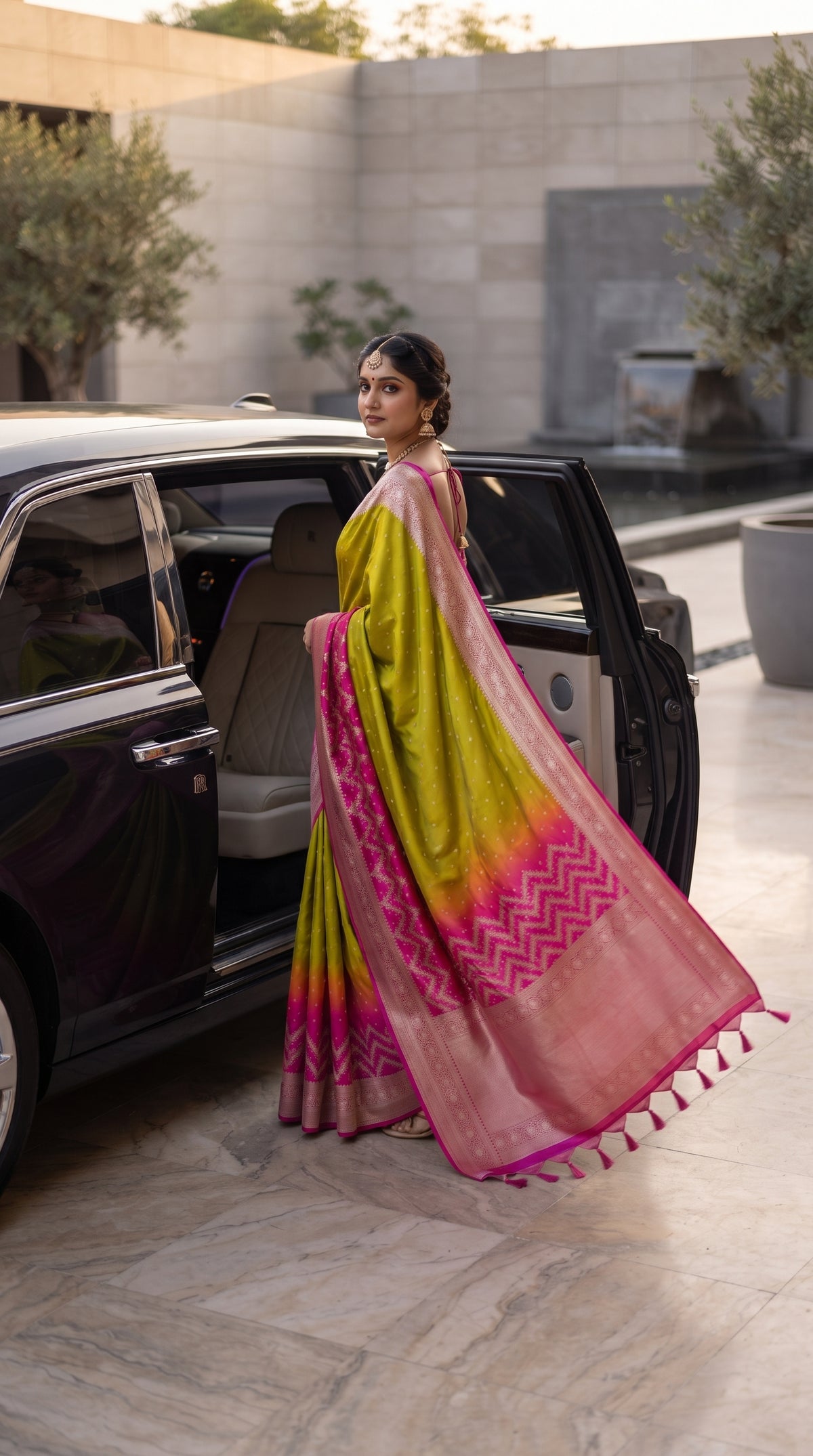 A three-quarter view of a woman stepping out of a luxury black car, elegantly highlighting the flowing magenta pallu with chevron zari work and tassels trailing behind her lime green Banarasi silk saree