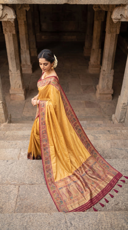 A high-angle shot of a woman descending ancient stone steps within a historical arcade hall, displaying the trailing multicolored Kani silk pallu with hand-tied matching tassels on her beige saree