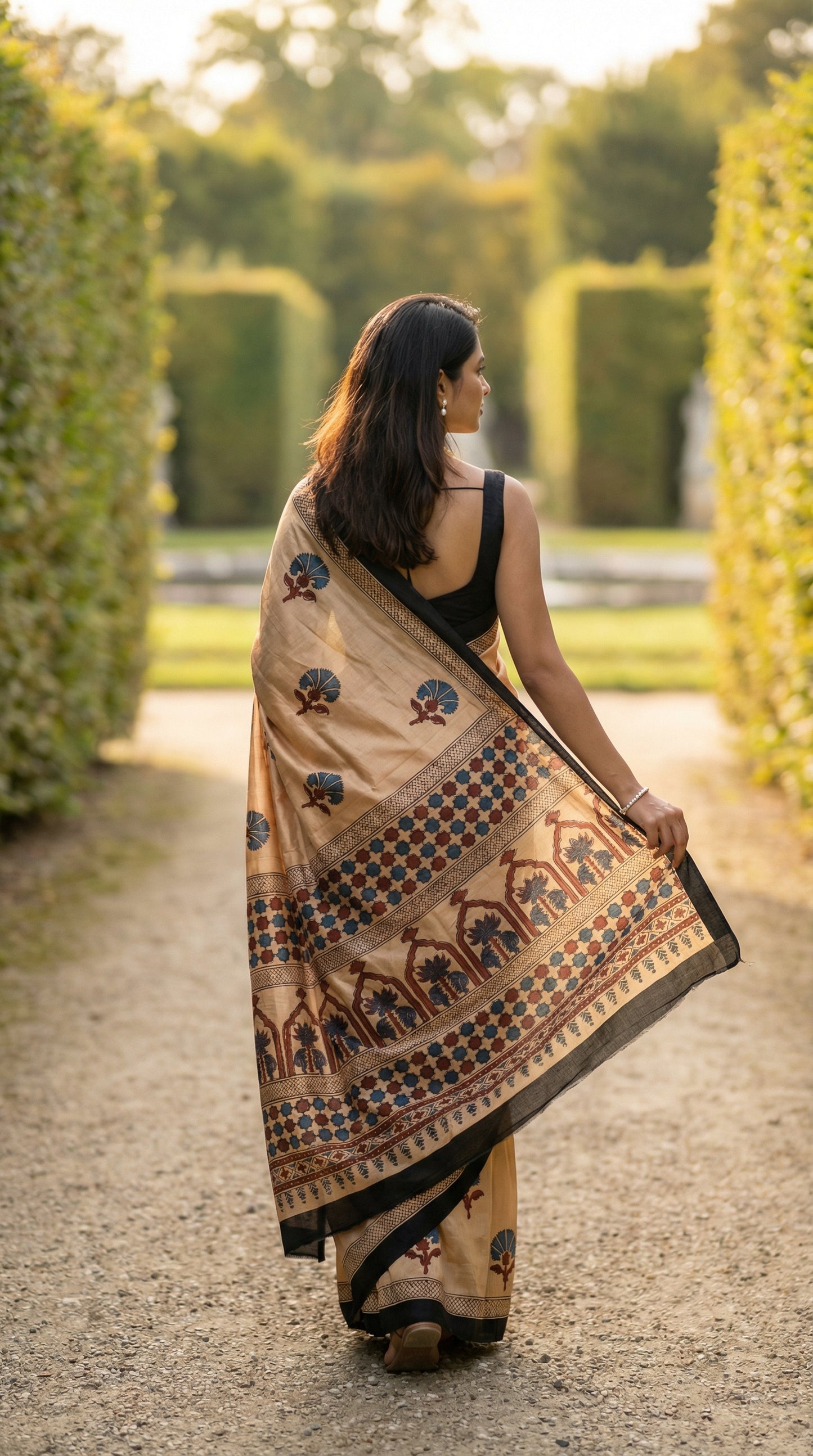 Woman walking outdoors wearing a Woman in ajrakh Modal Silk Saree – Beige with Black Borders and Blue-Maroon Pallu saree.
