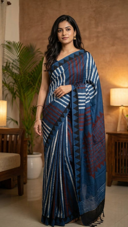 Woman wearing a Ajrakh Modal Silk Saree – Deep Blue with Maroon Chevron & Triangular Border Motifs in a room with lamps and plants.