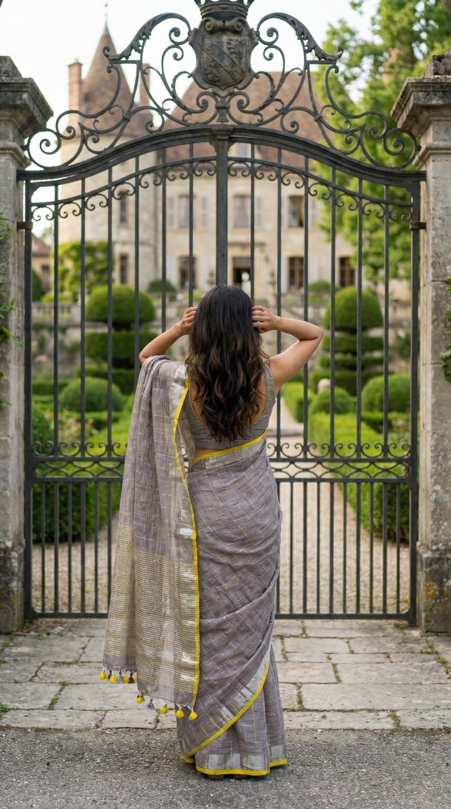 Woman in a ash-grey-cotton-linen-saree, standing in front of an ornate metal gate.
