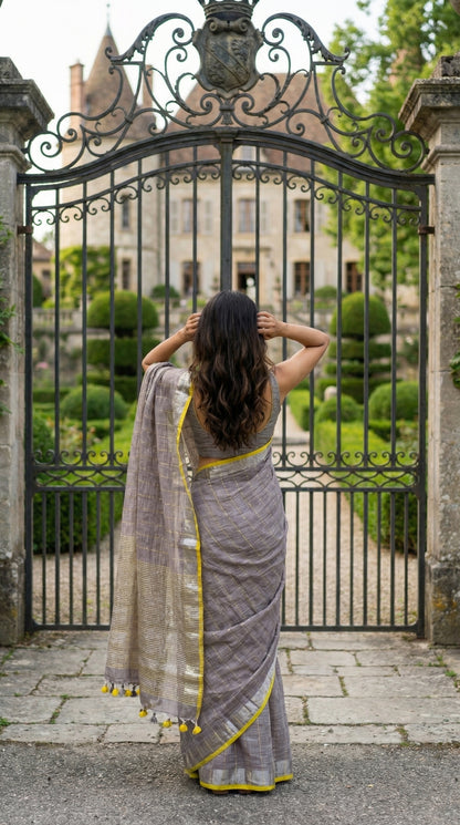 Woman in a ash-grey-cotton-linen-saree, standing in front of an ornate metal gate.
