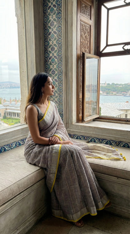 Woman in a ash-grey-cotton-linen-saree, sitting on a window sill with a scenic view.