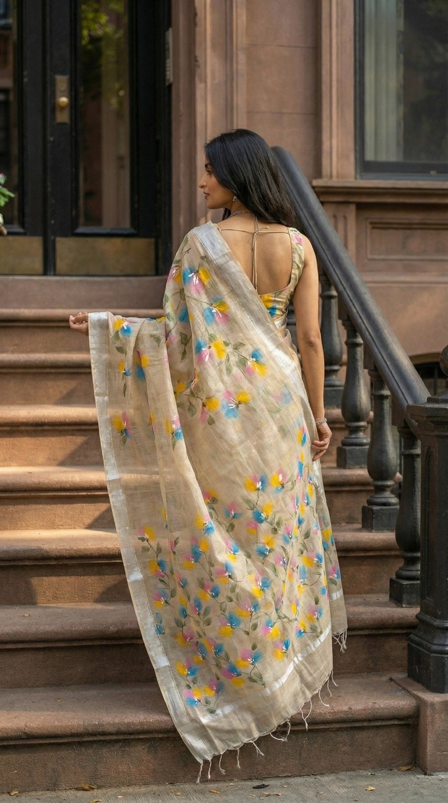 Woman wearing a beige-hand-painted-cotton-saree, standing on outdoor steps