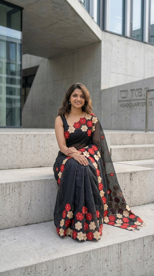 Woman in a black-mirror-work-kota-saree, sitting on steps in front of a modern building.