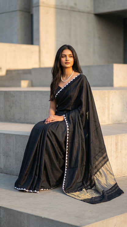 Woman in a black-modal-silk-saree-lagdi-patta-pallu, sitting on concrete steps.