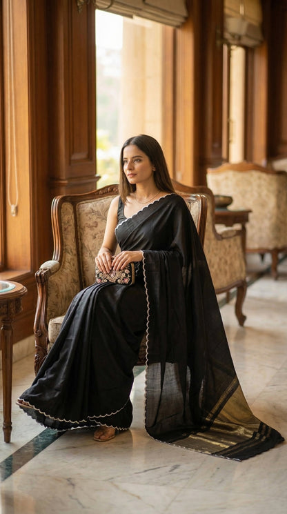 Woman in a black-modal-silk-saree-lagdi-patta-pallu, sitting on an ornate chair in a grand room.