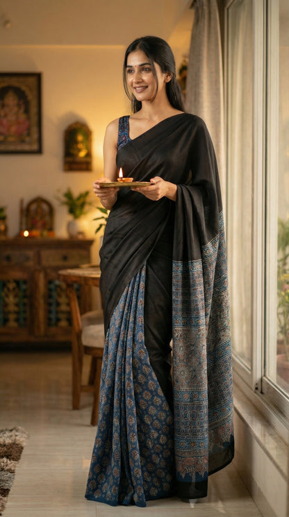 Woman in a black modal silk saree with intricate blue Ajrakh border detailing, holding a plate indoors.